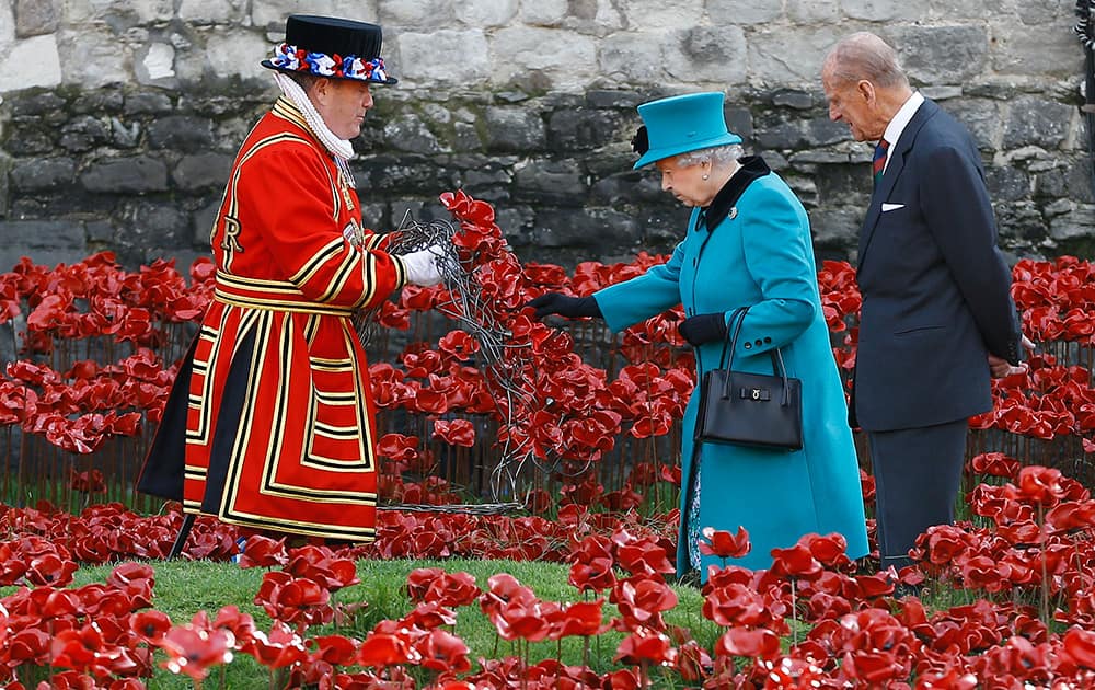 Britain's Queen Elizabeth II, alongside the Duke of Edinburgh, touches a wreath held by a Yeoman Warder before it is laid in the field of ceramic poppies at The Tower of London.