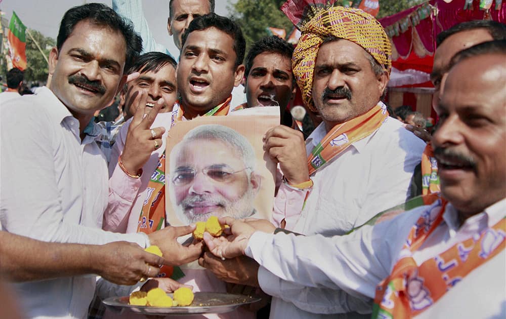 BJP workers offer sweets to a poster of PM Narendra Modi while celebrating the party victory in the Assembly polls in Gurgaon.