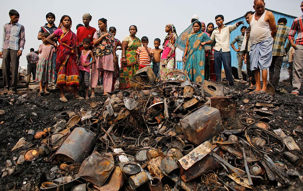 Indians stand near a pile of utensils that lay covered in ash after a fire at a slum area in New Delhi.