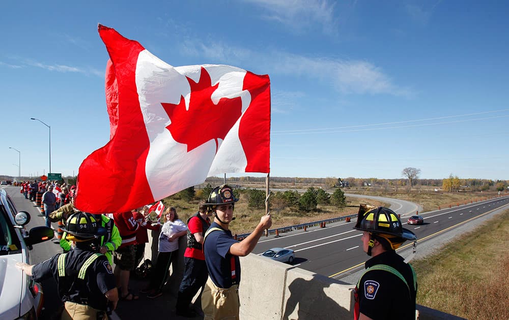 An Ottawa firefighter waves a Canadian Flag as crowds wait on an overpass at the Veterans Memorial Highway for a procession transporting the body of Cpl. Nathan Cirillo to pass by in Ottawa.