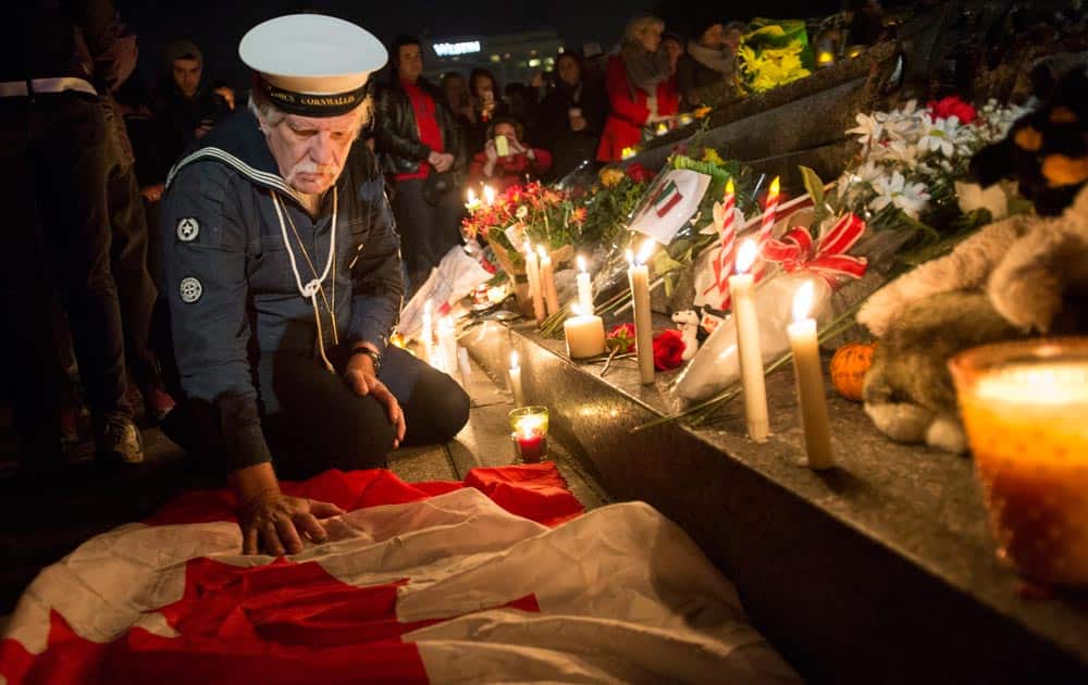 Richard Vallance Janke, a former member of the navy, touches the Canadian flag after lighting a candle at the Tomb of the Unknown Soldier at the National War Memorial during a candlelight vigil in Ottawa.
