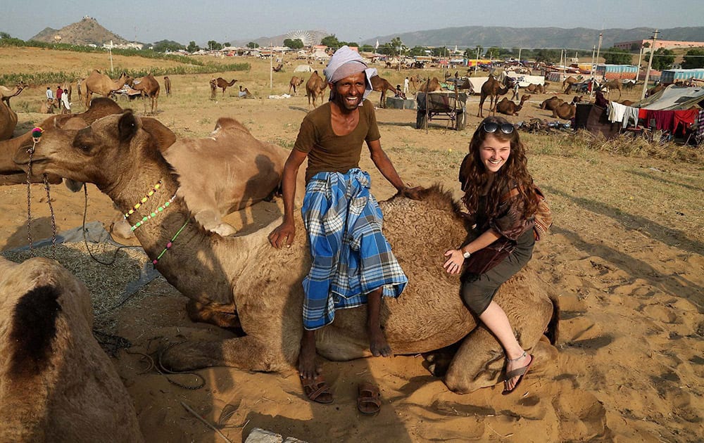 A foreign tourist sits on a camel for photograph during the Camel Fair in Pushkar.