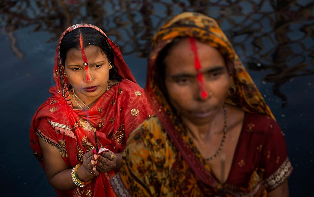 Hindu women, vermillion powder on their foreheads, perform rituals at sunset to mark Chhath Puja festival in New Delhi.