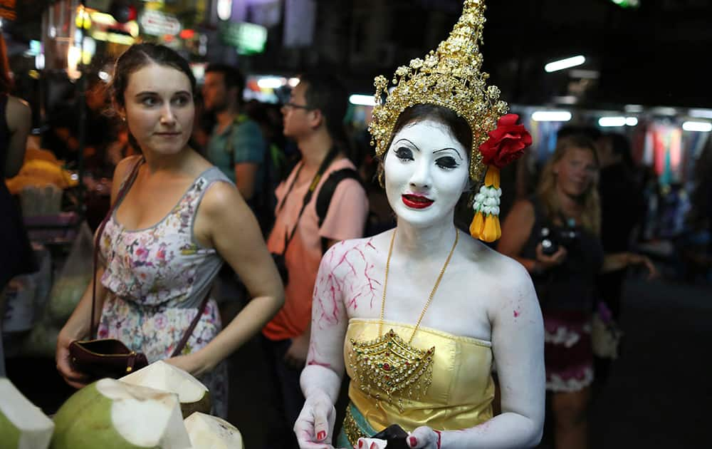 A tourist looks at a Thai woman dressed in a ghost costume for Halloween buying coconut in Bangkok.