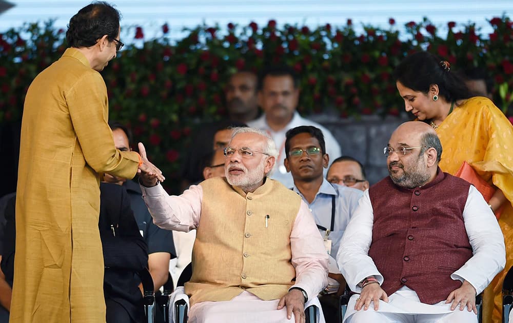 Prime Minister Narendra Modi shakes hands with Shiv Sena chief Uddhav Thackeray as BJP President Amit Shah looks on during the swearing-in ceremony of new Maharashtra government in Mumbai .