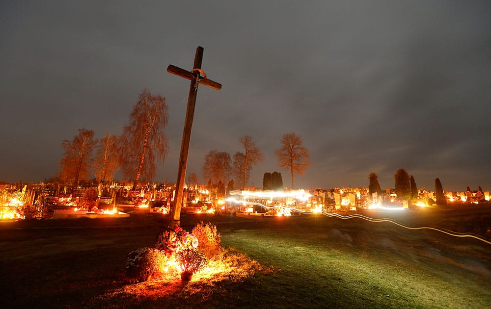 In this photo taken with a long exposure, people walk past graves illuminated by candles at a cemetery in the village of Boruny, 100 kilometers (62 miles) northwest of Minsk.