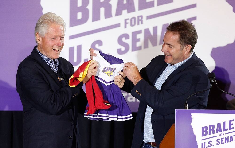 US Sen. candidate Bruce Braley, right, gives an Iowa State sleeper and Northern Iowa dress to President Bill Clinton for his granddaughter at Bruce, Blues and BBQ event at the Electric Park Ballroom in Waterloo, Iowa.