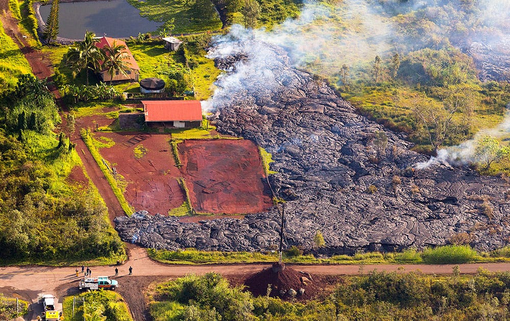 This photo released by The County of Hawaii via Ena Media Hawai’i/Blue Hawaiian Helicopters shows lava flow from the Kilauea Volcano near a residential structure in Pahoa, Hawaii.