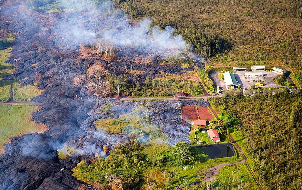 This photo released by The County of Hawaii via Ena Media Hawai’i/Blue Hawaiian Helicopters shows lava flow from the Kilauea Volcano near a residential structure in Pahoa, Hawaii.