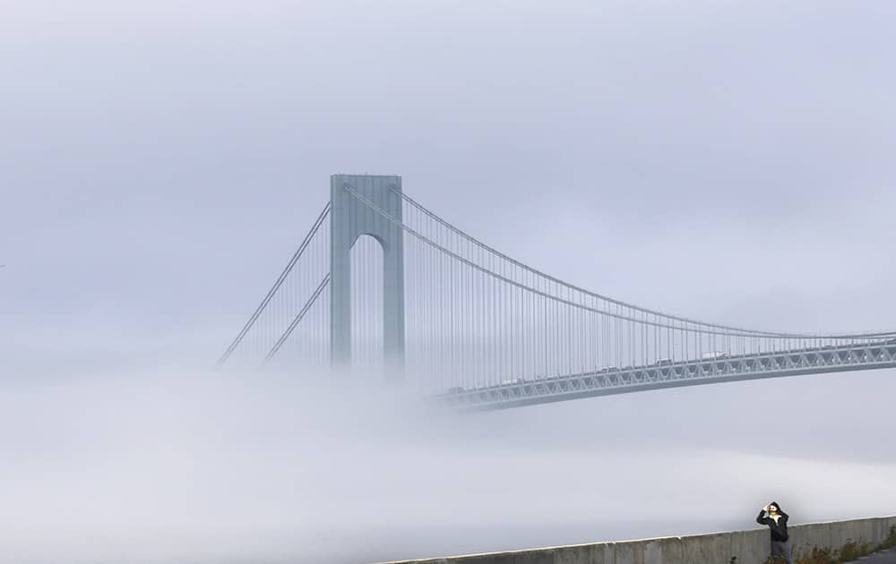 A man stops to take a picture of the foggy landscape in front of the Verrazano-Narrows Bridge in New York.