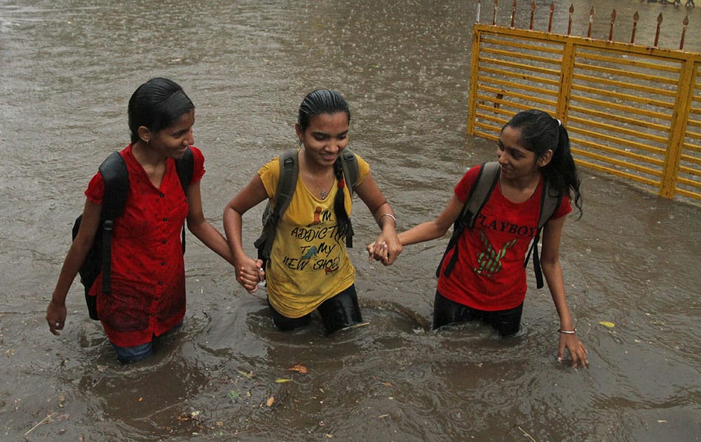 Indian girls hold hands and wade through a waterlogged street caused by unseasonal rainfall in Ahmadabad, India.