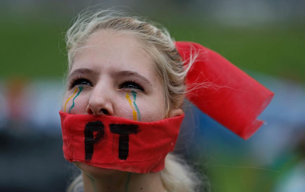 A demonstrator who wears a red scarf covering her month, imprinted with the ruling Workers' Party acronym, and lines in her country's national colors drawn on her face to symbolize a stream of tears, takes part in a protest march demanding the impeachment of re-elected Brazilian President Dilma Rousseff, over an alleged scheme of corruption that siphoned money from the state-owned oil company Petrobras, in Brasilia, Brazil.