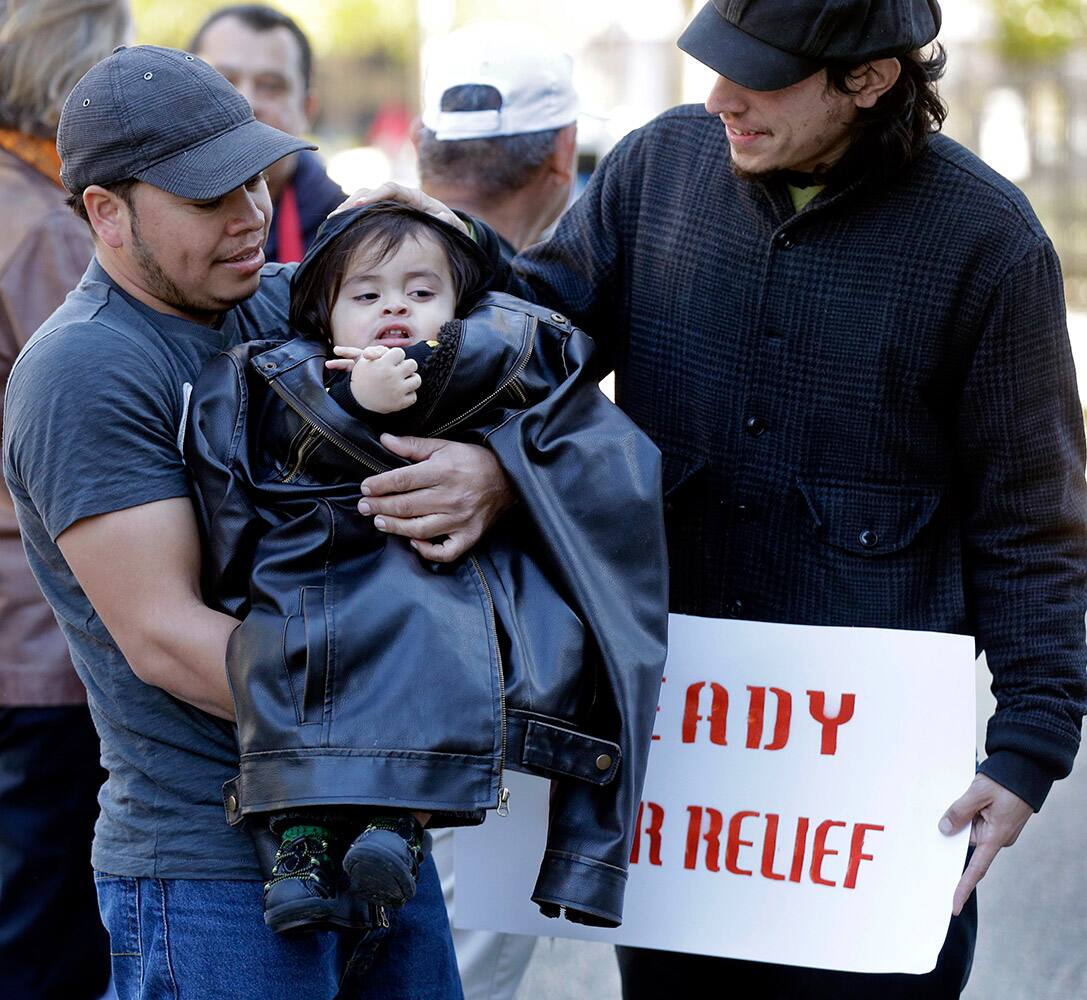Denis Cherino, of Honduras, holds his 17-month old son, also named Denis Cherino, wrapped in his coat, along with Arnulfo Manriquez, right, as immigrants and activists hold a protest outside the US Citizenship & Immigration Service office in New Orleans.