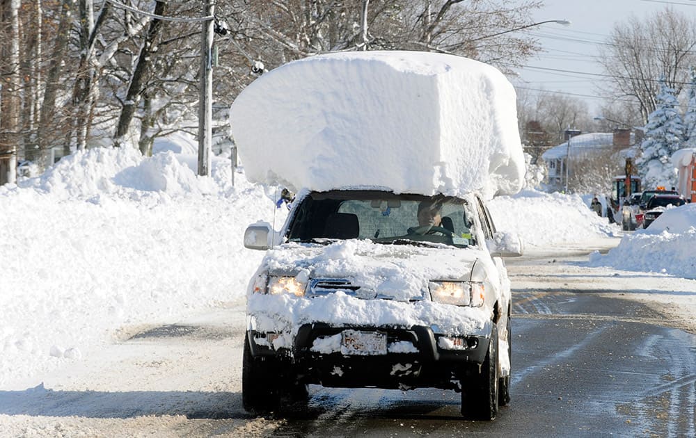 A vehicle, with a large chunk of snow on its top, drives along Route 20 after digging out after a massive snow fall in Lancaster, New York.