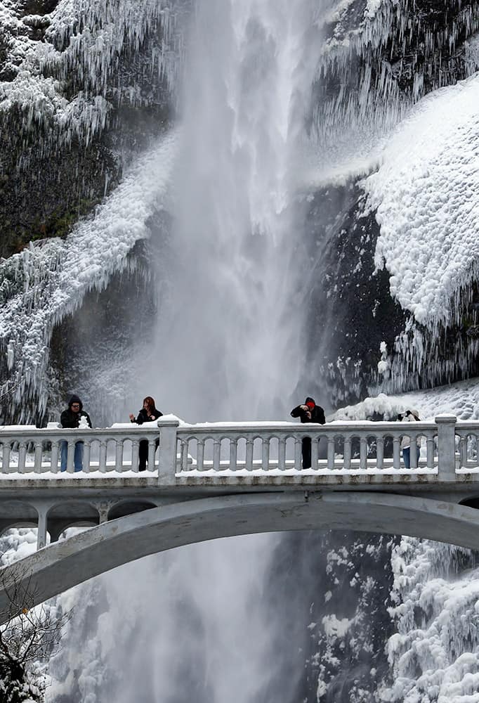 Vistors play with snow and take photos against the backdrop of ice and snow covered walls at Multnomah Falls in the Columbia River Gorge near Bridal Veil, Ore.