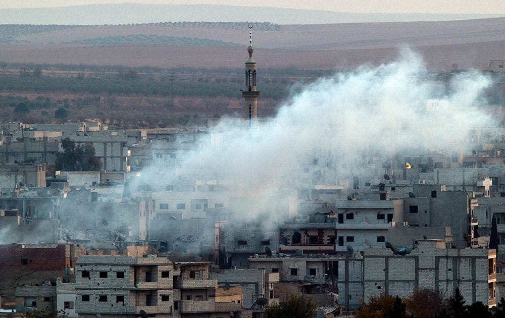 A minaret in Kobani is partly obscured by smoke after a mortar strike during fighting between Islamic state group forces and Kurdish fighters, seen from a hill outside Suruc, on the Turkey-Syria border.