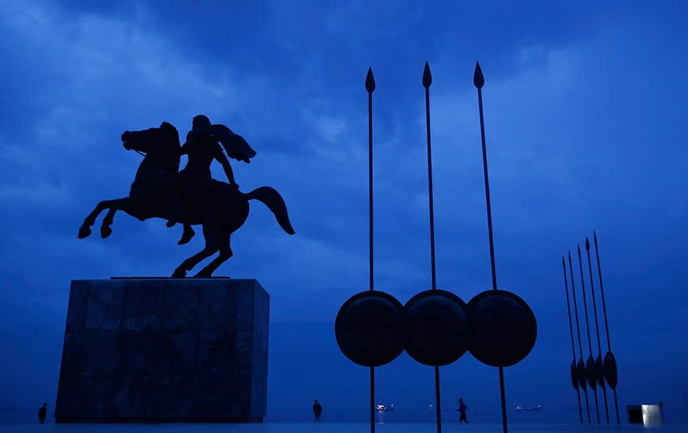 A modern bronze statue of Alexander the Great on his famous horse Bucephalus, flanked by copies of round shields and the Macedonian infantry's terrible Sarissa pike, stands under the cloudy sky of the northern port city of Thessaloniki, Greece.