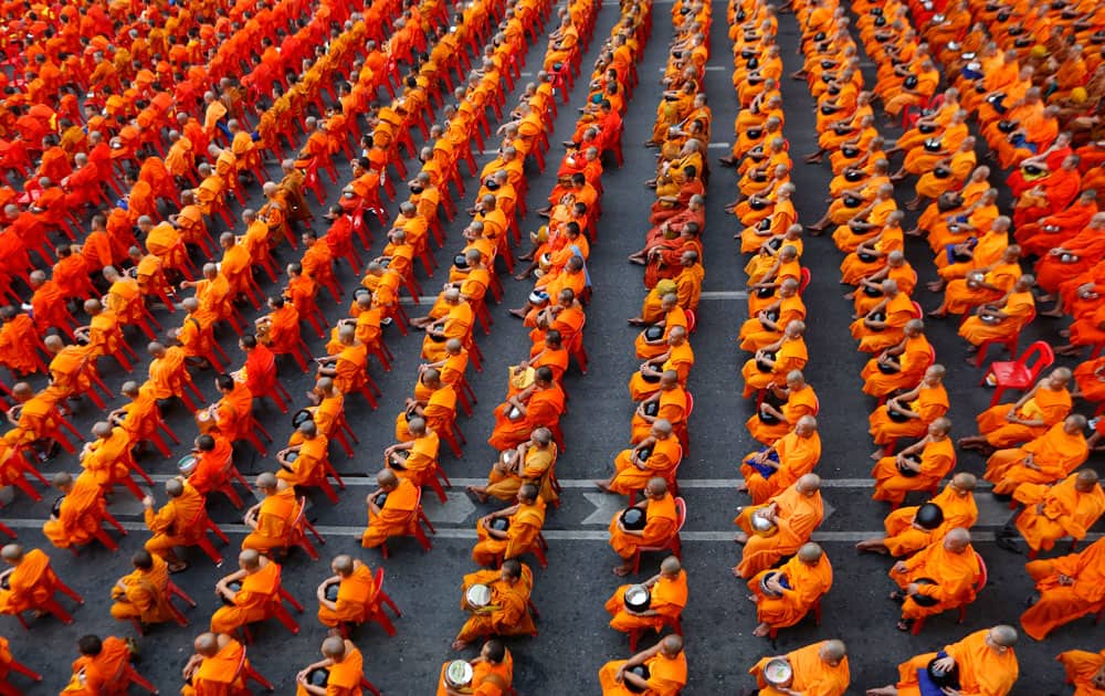 Buddhist monks carrying bowls sit on chairs before civilians drop dried food into the bowls in Bangkok, Thailand.