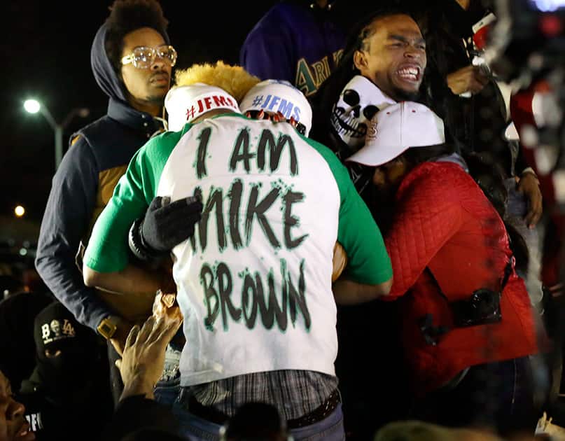 Lesley McSpadden, the mother of Michael Brown, second from left standing on the top of a car, hugs an unidentified man, wearing an I am Mike Brown shirt, as she listens to the announcement of the grand jury decision, in Ferguson.