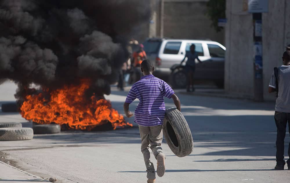 A young man runs with a found tire to add to a burning barricade during a protest demanding the resignation of President Michel Martelly in Port-au-Prince, Haiti.