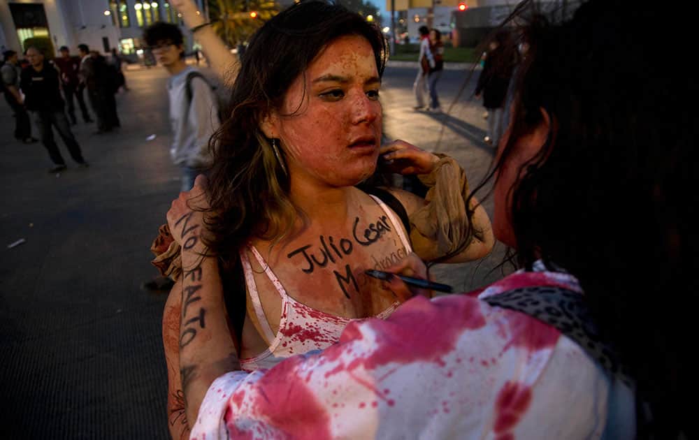 A protester gets the name of Julio Cesar Mondragon, a student that was savagely killed on the day that 43 students went missing, painted on her chest as she participates in a march in Mexico City.