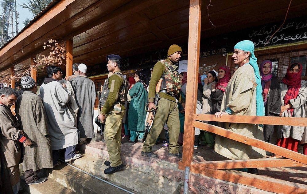 Security jawans stand guard as voters wait to cast their votes for Assembly elections at a polling station in Handwara district of Jammu and Kashmir on Tuesday. 18 assembly segments went to polling in the second phase of elections in the state.