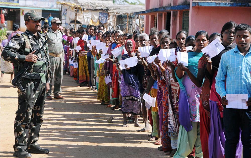 A security person stands guard as voters wait to cast their votes for assembly elections outside a polling station at Karra, Khunti near Ranchi.