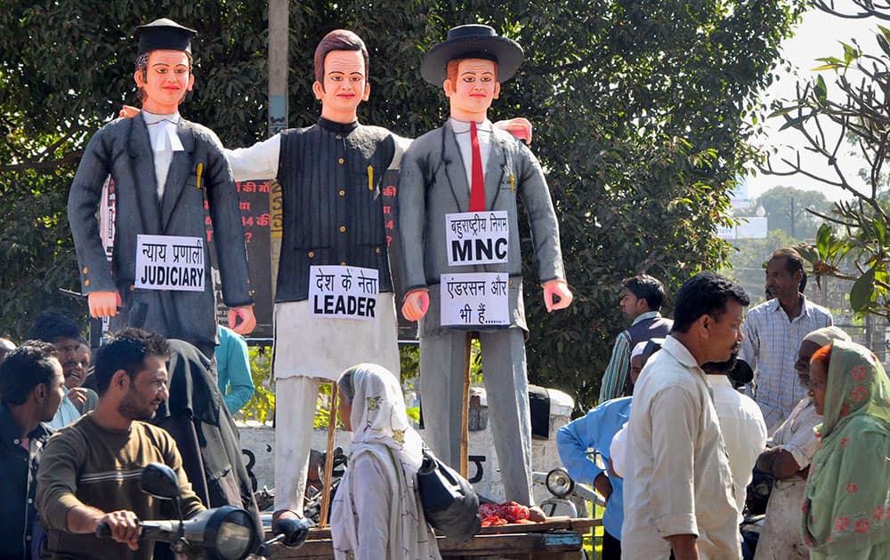 Indians walk near the effigies representing the judiciary, Indian politician and an MNC head, prepared by Bhopal Gas Peedith Mahila Udyog Sangthan, or Gas Affected Women Workers’ Union, on the 30th anniversary of the Bhopal gas tragedy in Bhopal, India.