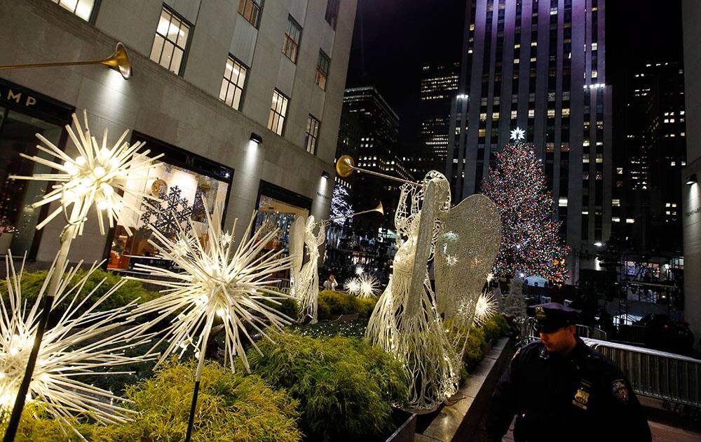 A police officer looks through shrubs in the Channel Gardens as the Rockefeller Center Christmas tree stands lit following a ceremony, in New York.