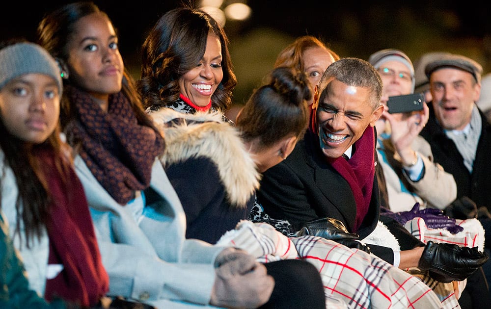 President Barack Obama, leans over to talk with his daughter Sasha as they sit with First Lady Michelle Obama and Malia and watch the performances at the National Christmas Tree lighting ceremony at the Ellipse near the White House in Washington.