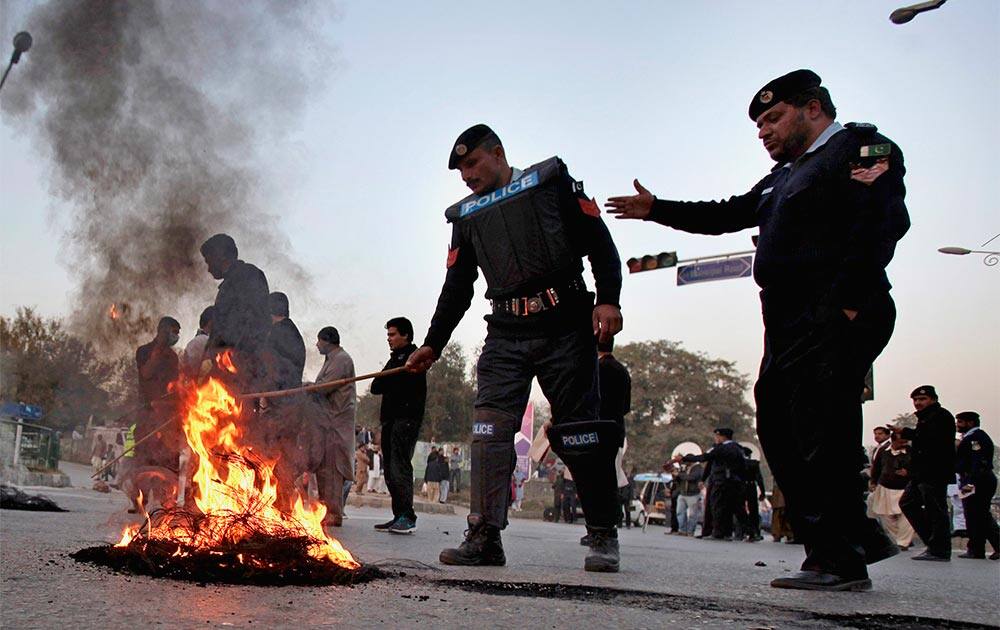 Pakistani police officers remove burning tires set on fire by supporters of cricketer star-turned-politician Imran Khan to protest against the killing of their colleague.