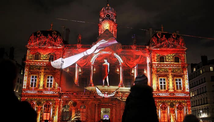 People attend a night light show illuminated on part of the city hall building of Lyon, central France,, as part of the Festival of Lights. Millions of visitors come into the city to watch the four-day event.