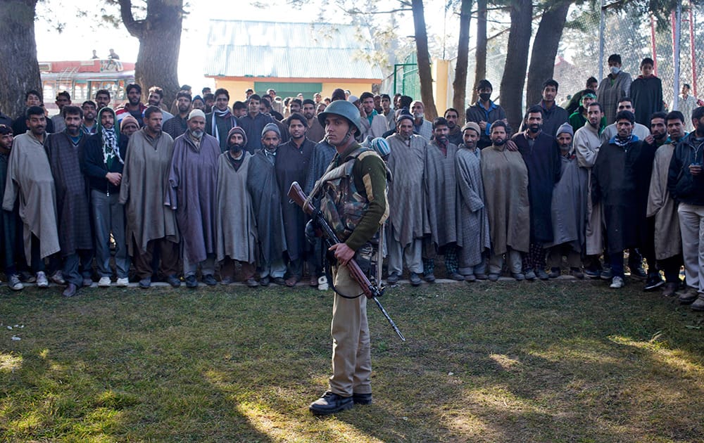 An Indian paramilitary soldiers stands guard as Kashmiri voters stand in queue as they wait outside a polling station during the third phase voting of the Jammu and Kashmir state elections in Monu village, about 55 kilometers south west of Srinagar, Kashmir.