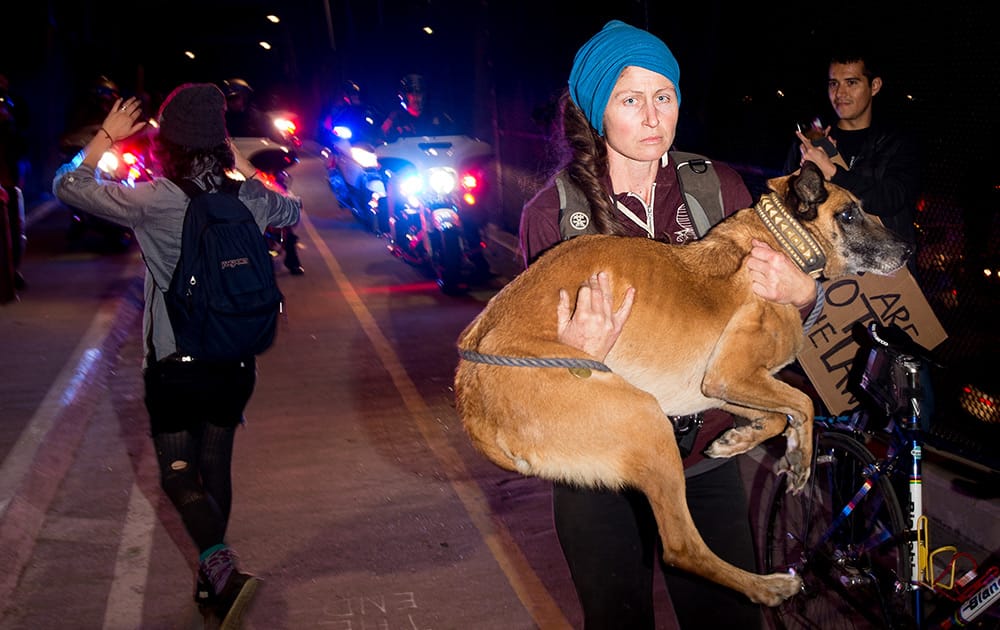 A woman carries her dog as police try to remove protesters, rallying against police violence, from a footbridge in Berkeley, Calif.