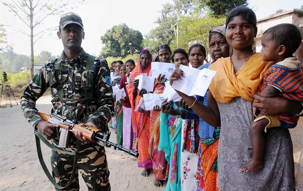 Security Personnels keep a strict vigil as the people stand in queue to cast their votes in the 3rd Phase of Jharkhand Assembly Election at Jonha village of Silli near Ranchi.