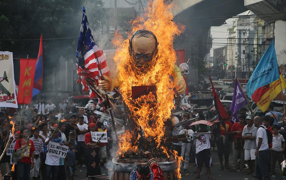 A man belonging to an indigenous tribe, foreground bottom, raises his clenched fist in front of a burning effigy of Philippine President Benigno Aquino III holding a mock U.S. flag as they mark International Human Rights Day outside the presidential Malacanang Palace in Manila, Philippines.