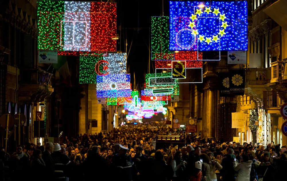 People stroll along Rome's Via del Corso main shopping street, lit up with Christmas decorations representing the world's flags