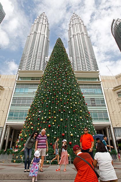 People stand in front of a giant Christmas tree on display against the Malaysia's landmark Petronas Twin Towers in Kuala Lumpur, Malaysia.