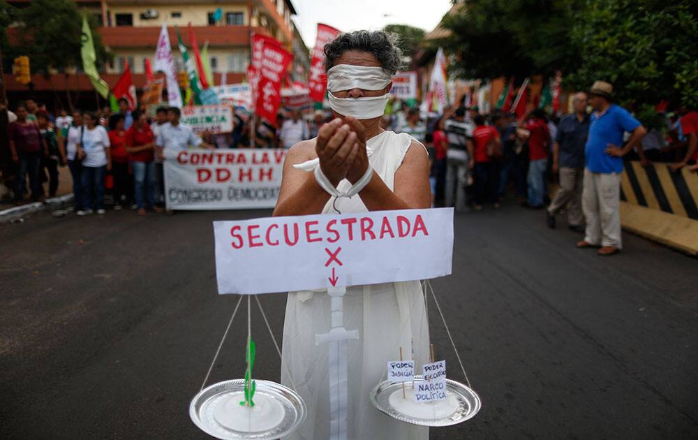 A woman symbolizing justice carries a sign that reads in Spanish 