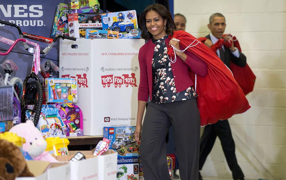 First lady Michelle Obama, followed by President Barack Obama, arrives carrying bags of gifts over their shoulders before helping sort toys and gifts for the Marine Corps' Toys for Tots Campaign, at Joint Base Anacostia-Bolling in Washington.