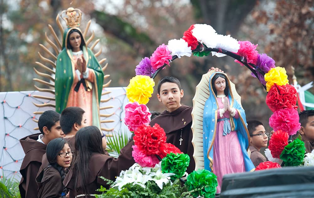 Alter servers ride on a float with two statues depicting the Our Lady of Guadalupe image during the annual St. Peter Claver Parish Virgen de Guadalupe parade in Tyler, Texas.