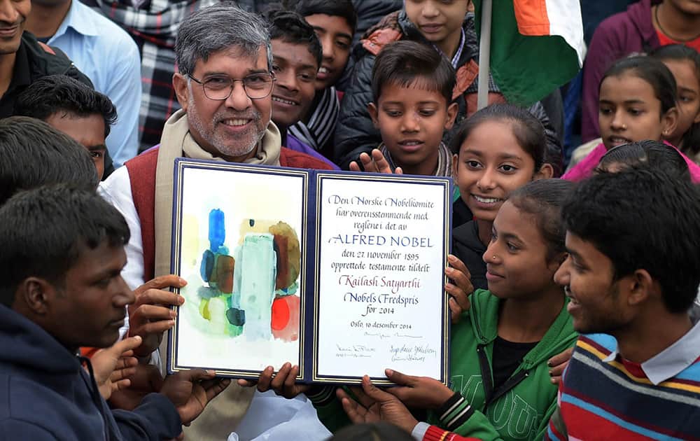 Nobel Peace Prize winner Kailash Satyarthi holds up his Nobel diploma as he poses with children after paying tribute at Raj Ghat in New Delhi.