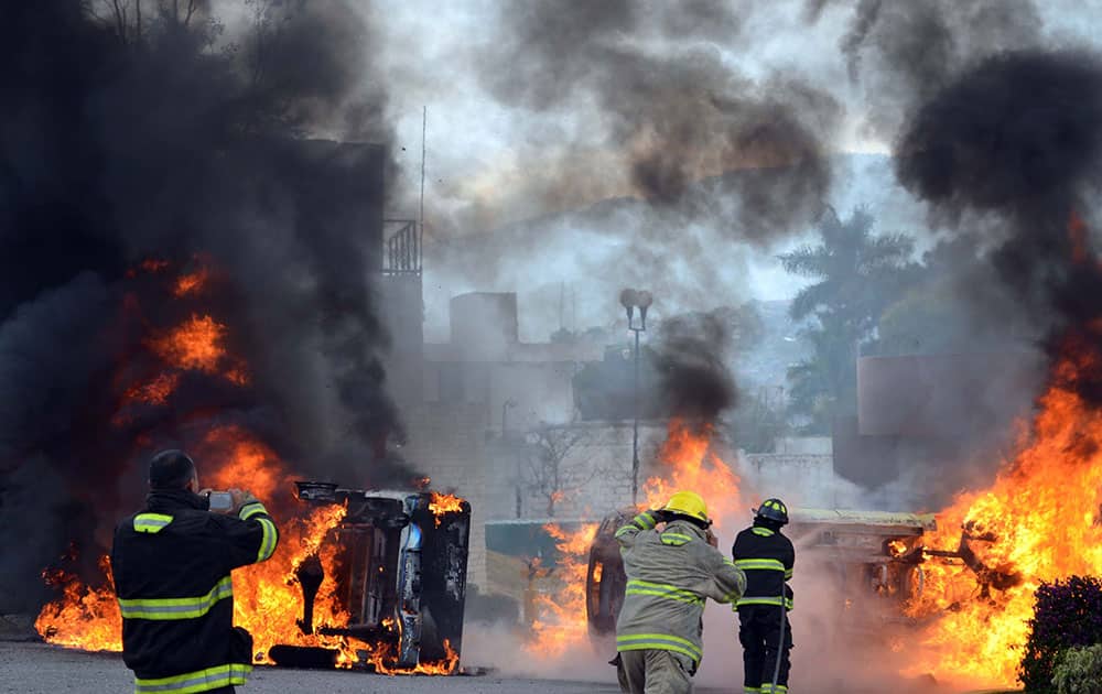 Firefighters attempt to put out the fire as vehicles burn at the entrance of the Guerrero police academy after being set alight by protesters at the state capital of Chilpancingo.