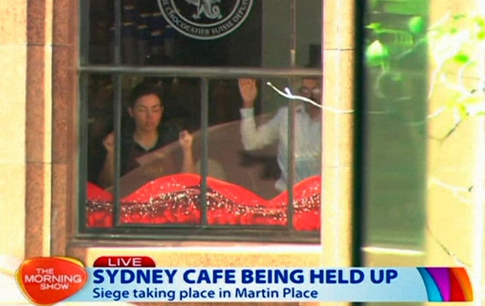This image taken from video shows people holding up hands inside a cafe in Sydney, Australia.