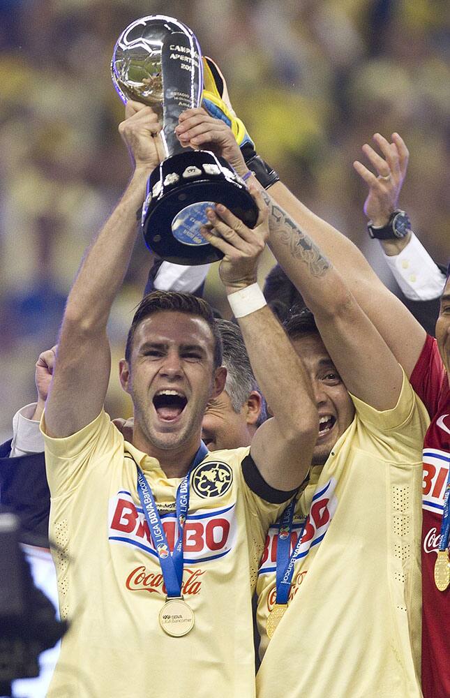 America's captain Miguel Layun, left, holds up the Mexican national soccer league trophy after defeating Tigres and the end of the Mexican league final soccer match in Mexico City.