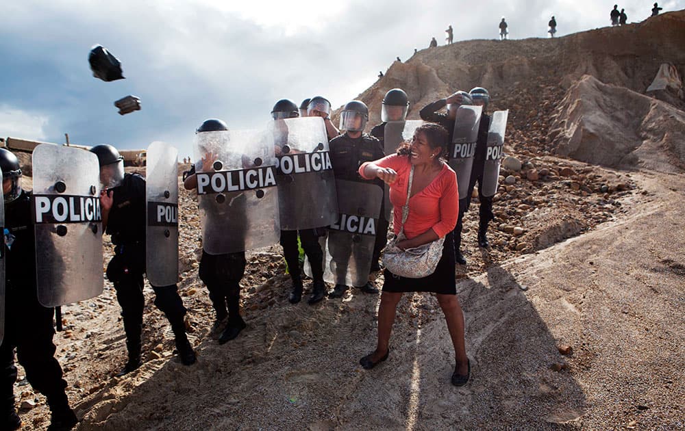 In this April 28, 2014 file photo, a woman throws a rock and a bag at police blocking her from getting home in the Huepetuhe district of the Madre de Dios region of Peru.