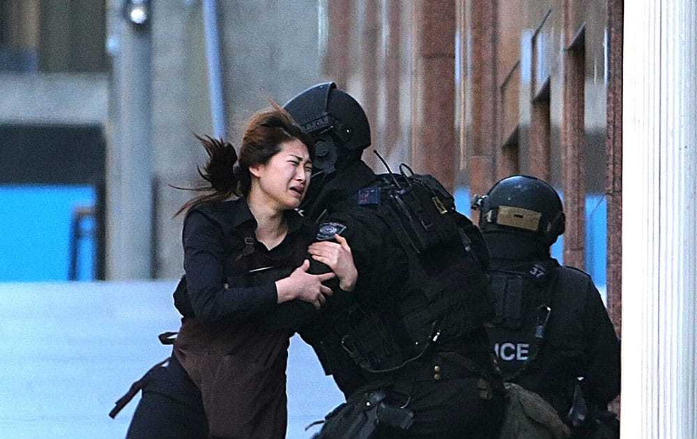 A hostage runs to armed tactical response police officers for safety after she escaped from a cafe under siege at Martin Place in the central business district of Sydney, Australia, Monday, Dec. 15, 2014. New South Wales state police would not say what was happening inside the cafe or whether hostages were being held. But television footage shot through the cafe's windows showed several people with their arms in the air. 