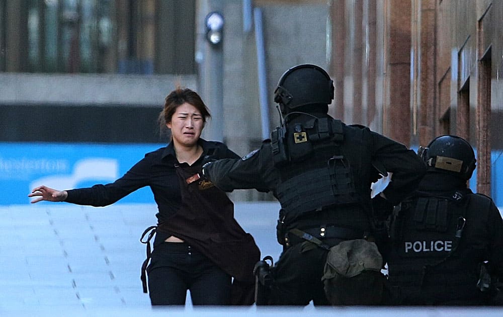 A HOSTAGE RUNS TO ARMED TACTICAL RESPONSE POLICE OFFICERS FOR SAFETY AFTER SHE ESCAPED FROM A CAFE UNDER SIEGE AT MARTIN PLACE IN THE CENTRAL BUSINESS DISTRICT OF SYDNEY, AUSTRALIA, MONDAY, DEC. 15, 2014. NEW SOUTH WALES STATE POLICE WOULD NOT SAY WHAT WAS HAPPENING INSIDE THE CAFE OR WHETHER HOSTAGES WERE BEING HELD. BUT TELEVISION FOOTAGE SHOT THROUGH THE CAFE'S WINDOWS SHOWED SEVERAL PEOPLE WITH THEIR ARMS IN THE AIR.