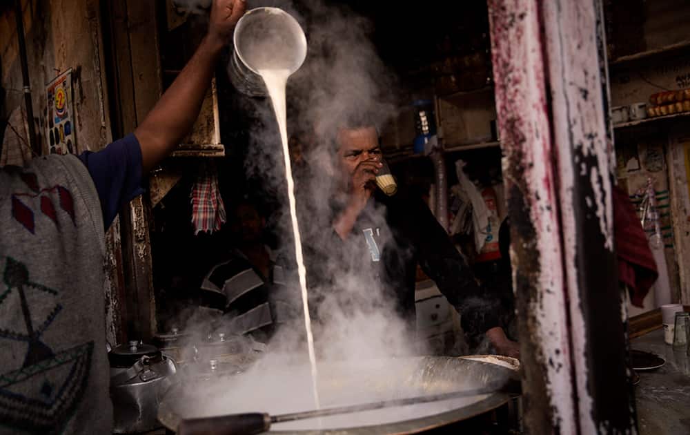 A man pours milk into a huge pot to prepare tea at a roadside stall in old parts of New Delhi. Cold wave conditions have intensified in the capital after scattered rains occurred in some parts of the city on Sunday, according to local reports.