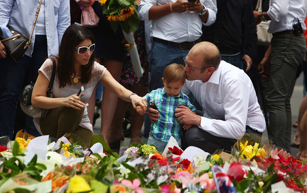 A father kisses his young son as they lay flowers in a makeshift memorial at Martin Place after shootings during a siege at a cafe in the central business district in Sydney.